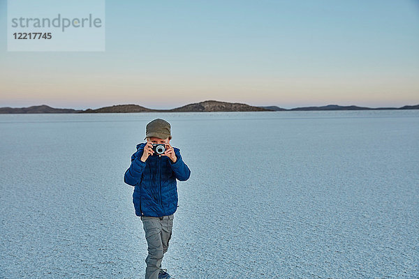 Junge steht auf Salinen und schaut durch die Kamera  Salar de Uyuni  Uyuni  Oruro  Bolivien  Südamerika