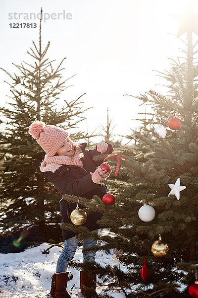 Mädchen legt Kugeln auf den Weihnachtsbaum im Wald