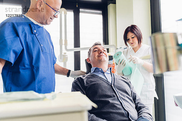 Männlicher Patient auf Zahnarztstuhl  neben ihm stehender Zahnarzt