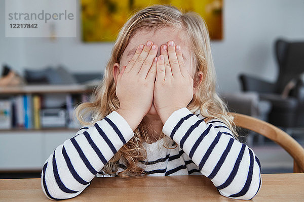 Porträt eines jungen Mädchens  am Tisch sitzend  das Gesicht mit Händen bedeckt