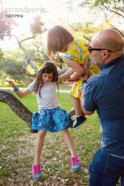 Vater und Töchter spielen im Freien  Töchter sitzen auf einem Baum