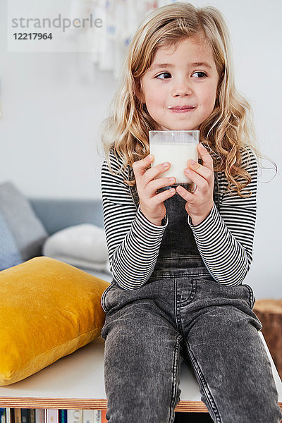 Junges Mädchen sitzt im Wohnzimmer und hält ein Glas Milch