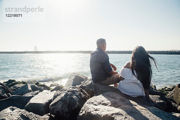 Paar auf Küstenfelsen sitzend  Blick auf Ansicht  Rückansicht