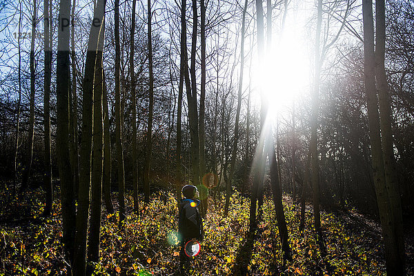 Junge steht im Wald und schaut durch Bäume auf die Sonne