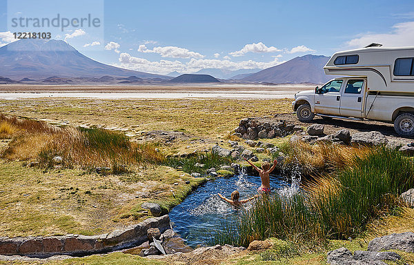 Zwei Jungen spielen im Wasserbecken neben einem geparkten Wohnmobil  Salar de Chiguana  Chiguana  Potosi  Bolivien  Südamerika