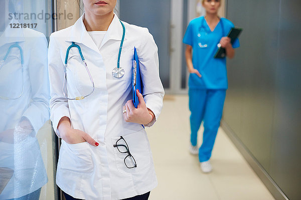 Im Krankenhausflur stehender Arzt  im Hintergrund gehender Chirurg  Mittelteil