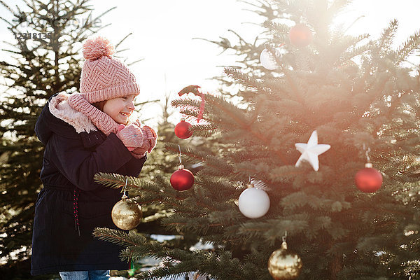 Mädchen betrachtet Kugeln am Waldweihnachtsbaum