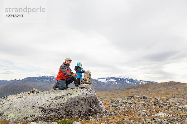 Männlicher Wanderer mit Sohn baut Steinhaufen in Berglandschaft  Jotunheimen-Nationalpark  Lom  Oppland  Norwegen