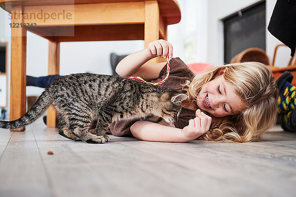 Junges Mädchen liegt auf dem Boden und spielt mit Hauskatze