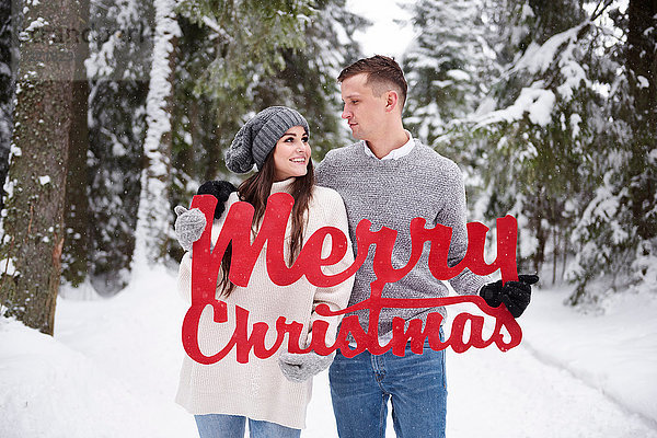 Junges Paar mit fröhlichen Weihnachtsworten im Schnee