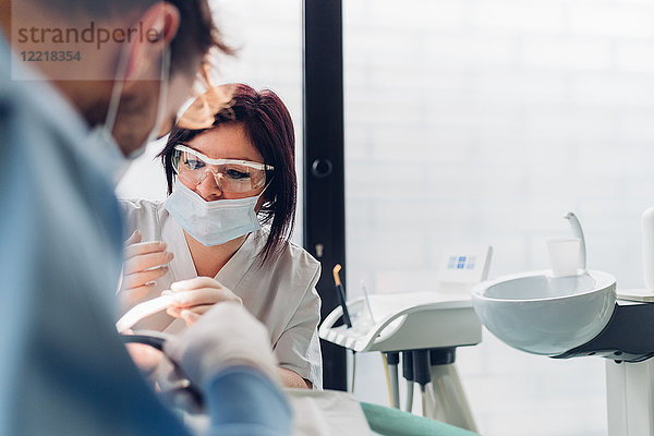 Zahnarzt und Zahnarzthelferin  die den Mund des Patienten untersuchen