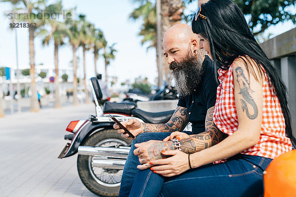 Älteres Hipster-Pärchen auf der Bank beim Betrachten eines Smartphones  Valencia  Spanien