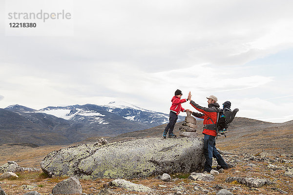Mann mit Söhnen über einem Steinhaufen in einer Berglandschaft  Jotunheimen-Nationalpark  Lom  Oppland  Norwegen