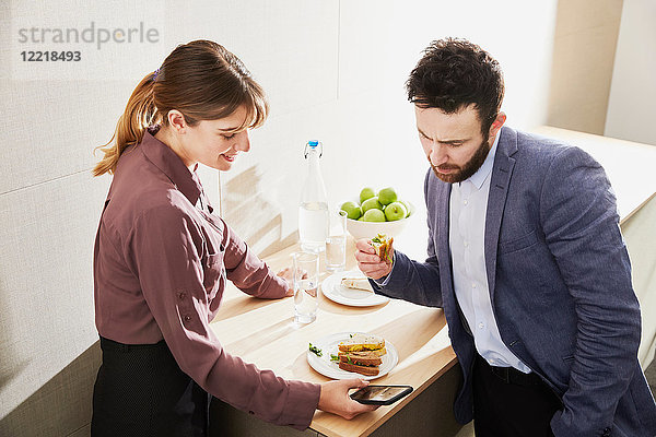 Geschäftsfrau und Mann schauen während des Arbeitsessens auf ein Smartphone