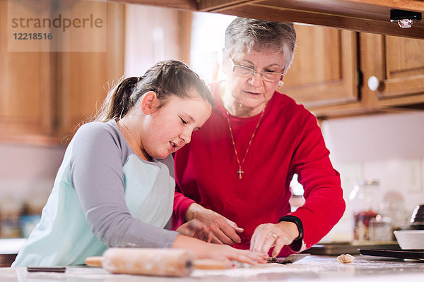Mädchen und Großmutter mit Ausstecher auf Teig an der Küchentheke