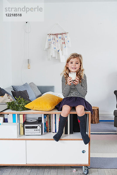 Junges Mädchen sitzt im Wohnzimmer und hält ein Glas Milch