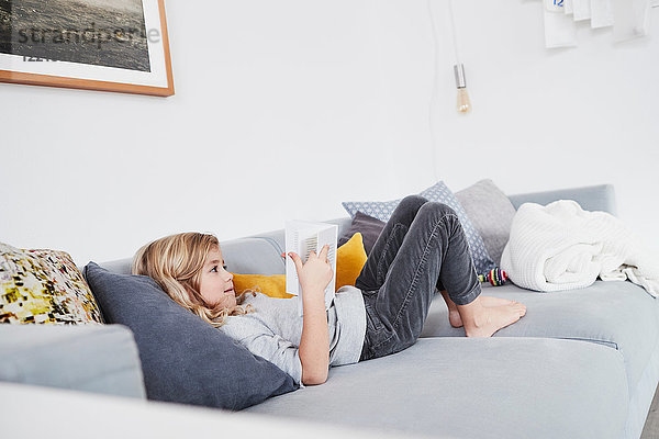 Junges Mädchen liegt auf Sofa  liest Buch