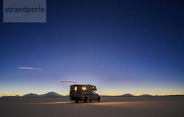 Freizeitfahrzeug  das in der Dämmerung über die Salinen fährt  Salar de Uyuni  Uyuni  Oruro  Bolivien  Südamerika