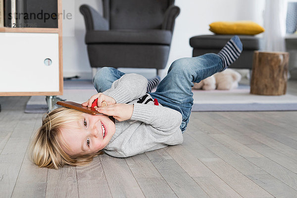 Junge Junge liegt auf dem Boden  hält das Smartphone ans Ohr und lächelt