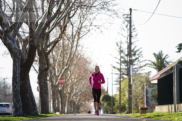 Junge Frau joggt in baumgesäumter Straße