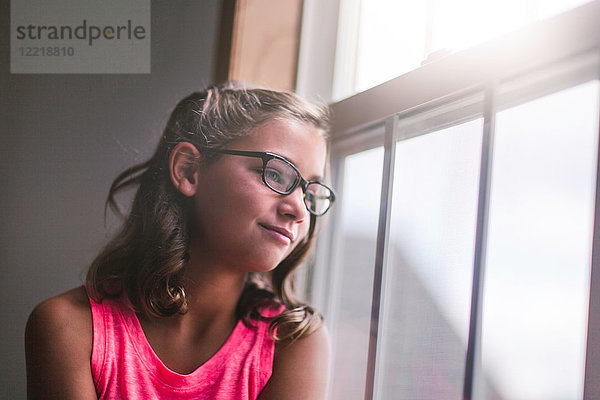 Junges Mädchen  das eine Brille trägt und aus dem Fenster schaut