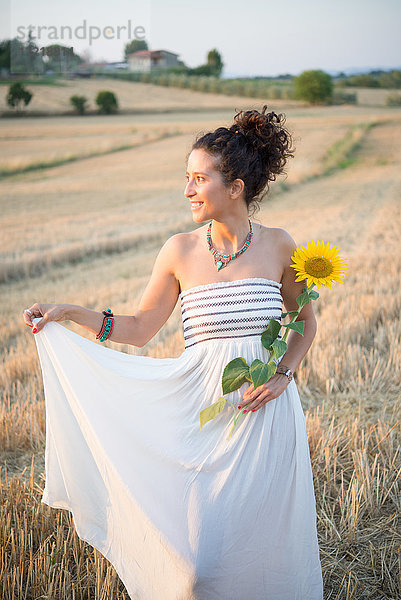 Bildnis einer mittelgroßen erwachsenen Frau  im Feld stehend  Sonnenblume haltend