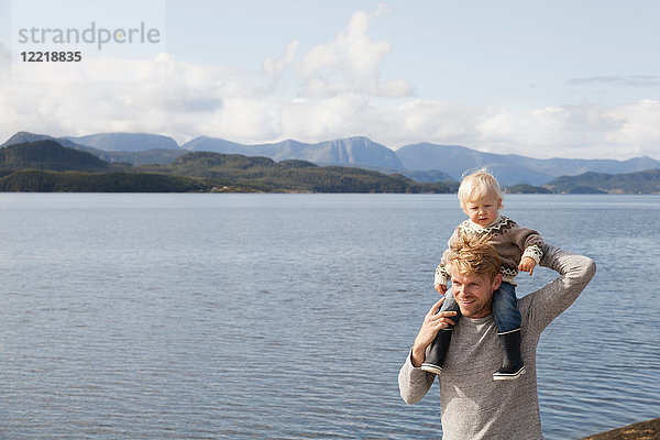 Mann  der seinem Sohn die Schulter zeigt  reitet am Fjord  Aure  More og Romsdal  Norwegen