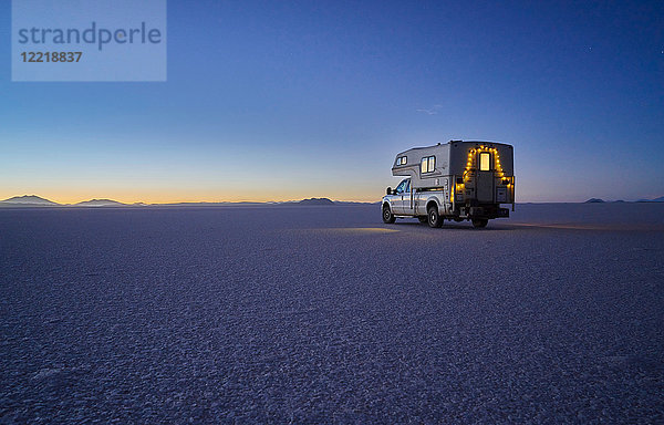 Freizeitfahrzeug  das in der Dämmerung über die Salinen fährt  Salar de Uyuni  Uyuni  Oruro  Bolivien  Südamerika