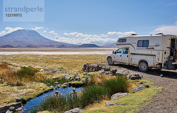 Zwei Jungen spielen im Wasserbecken neben einem geparkten Wohnmobil  Salar de Chiguana  Chiguana  Potosi  Bolivien  Südamerika