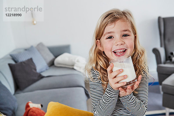 Porträt eines jungen Mädchens  das im Wohnzimmer sitzt  ein Glas Milch hält und lächelt