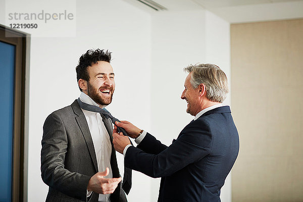 Leitender Geschäftsmann befestigt die Krawatte seines Kollegen im Amt
