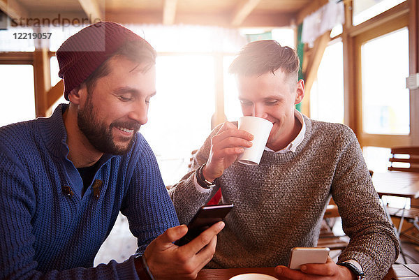 Junge Männer lächeln über Textnachrichten auf Mobiltelefonen