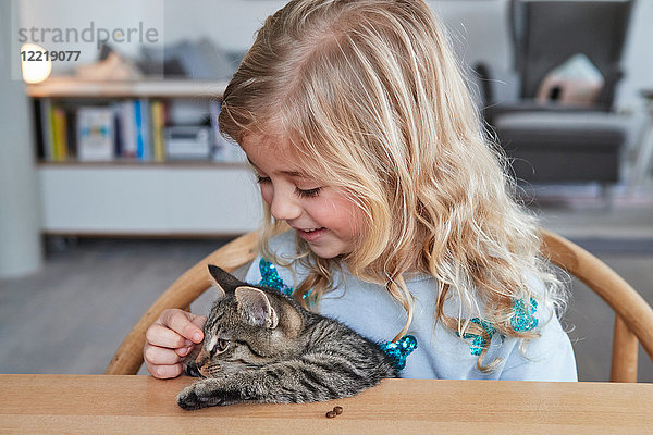 Porträt eines jungen Mädchens  das am Tisch sitzt und seine Katze streichelt