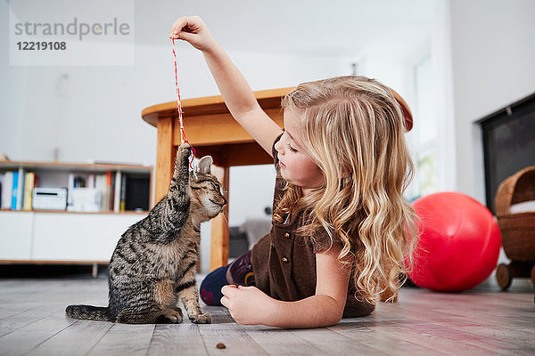 Junges Mädchen liegt auf dem Boden und spielt mit Hauskatze