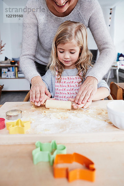 Mutter hilft Tochter beim Ausrollen des Plätzchenteigs auf dem Küchentisch  Mittelteil