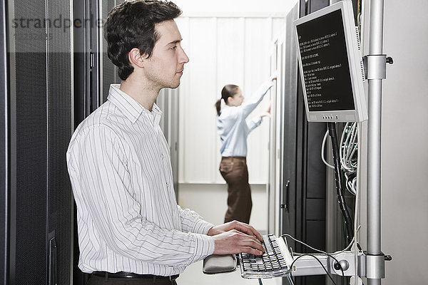 Ein männlicher Computertechniker  der in einem Gang mit Serverschränken in einer Computer-Serverfarm steht