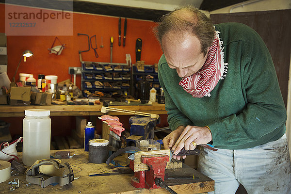 Ein Messermacher in einer Werkstatt  der die Klinge eines Küchenmessers vorsichtig in eine Klemme auf einer Werkbank legt.