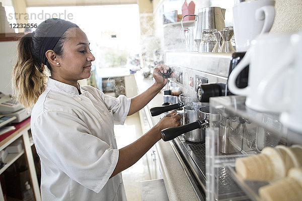 Hispanische Frau  die in einem Süßwarengeschäft an einer Espressomaschine arbeitet.
