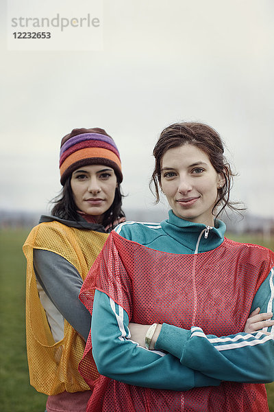 Porträt von zwei kaukasischen Frauen in Sportkleidung mit den Startnummern der gegnerischen Mannschaften und Wollmützen nebeneinander.