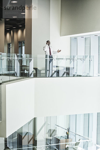 Schwarzer Geschäftsmann am Telefon  der in der Lobby eines großen Geschäftszentrums steht.
