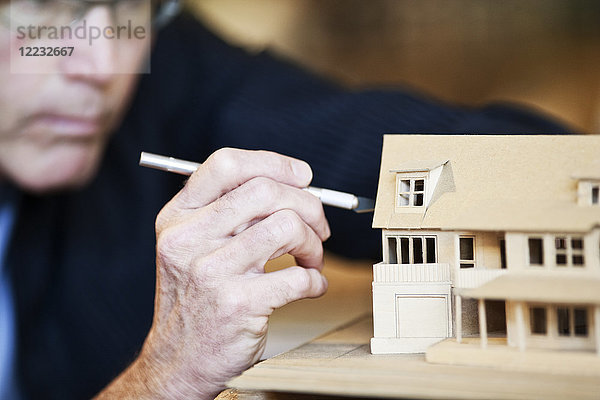 Kaukasischer männlicher Architekt  der an einem maßstabsgetreuen Modell eines neuen Hauses arbeitet.
