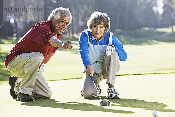 Älteres Ehepaar bespricht die Richtung des Putts auf dem Grün eines Golfplatzes.
