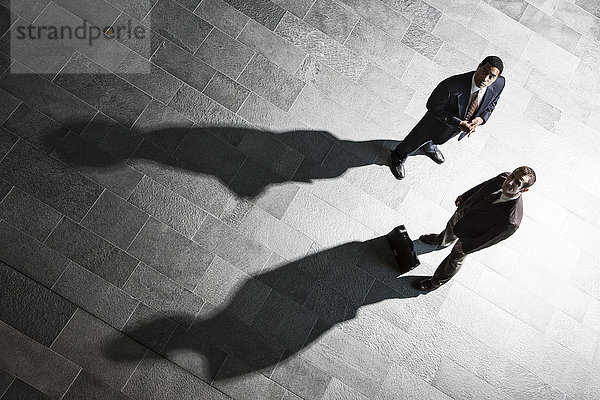 Blick von oben auf zwei Geschäftsleute und Schatten auf dem Boden einer Geschäftslobby.