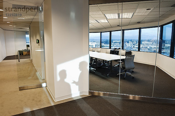 Schatten von zwei Geschäftsleuten an der Wand vor einem Konferenzraum eines Unternehmens.