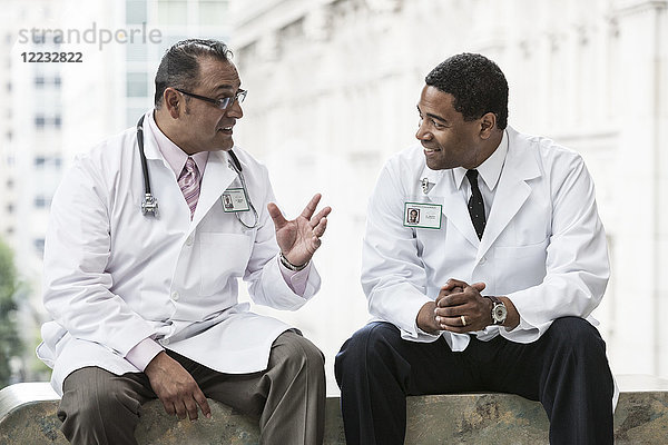 Schwarze und hispanische männliche Ärzte besprechen einen Fall in einem Krankenhausflur.