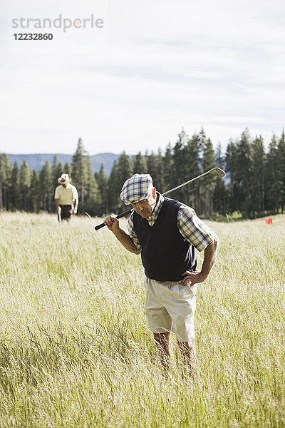 Älterer Golfspieler auf der Suche nach einem Golfball  der auf dem Golfplatz in ein schweres Rough geflogen ist.