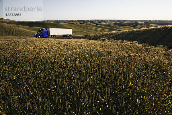 kommerzieller Lastwagen  der bei Sonnenuntergang durch Weizenfelder im Osten Washingtons  USA  fährt.