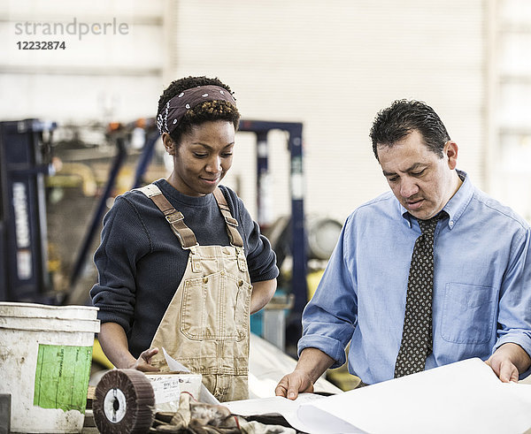 Ein spanischer Manager und eine schwarze Fabrikarbeiterin besprechen Projektpläne in einer Blechfabrik.