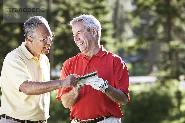 Zwei ältere Freunde lachen über einen Golfscore auf einem örtlichen Golfplatz.