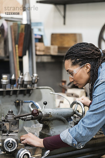 Frau mit Schutzbrille steht in einer Metallwerkstatt und arbeitet an einer Maschine.